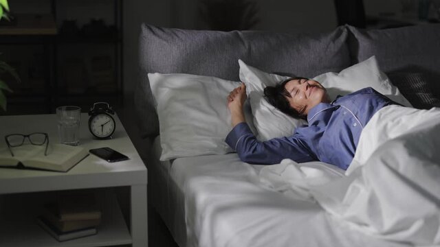 Happy relaxed woman stretching in bed while waking up. Pleasant middle aged lady in pajamas enjoying good morning time at home.