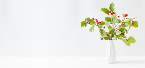 Home interior with decor elements. Red berries and green leaves in a vase on a light background