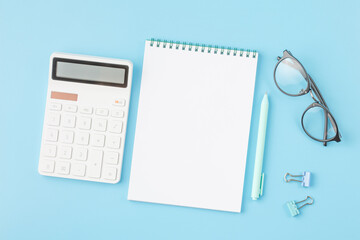 Office desk with calculator, notepad and glasses.