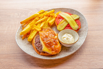 Delicatessen burger menu with pickled cucumbers, sliced tomato, onion marmalade, beef, goat cheese, brioche bread, bowl of mayonnaise and homemade fries