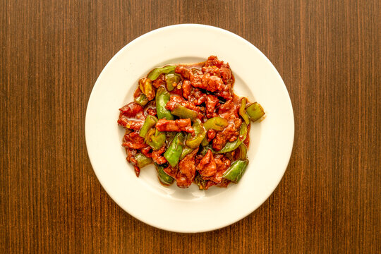 Top view image of wok-fried beef strips with green peppers on a white plate cooked by a Chinese chef