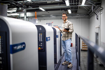 Portrait of professional graphic designer or engineer checking production on printing machine in...