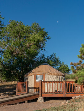 Yurt Surrounded by Trees with Waning Moon in Blue Sky