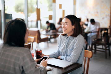 Teamwork. Two cheerful Asian young women meeting at cafeteria.
