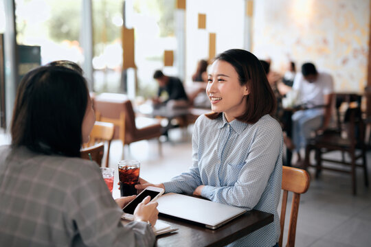 Teamwork. Two cheerful Asian young women meeting at cafeteria.