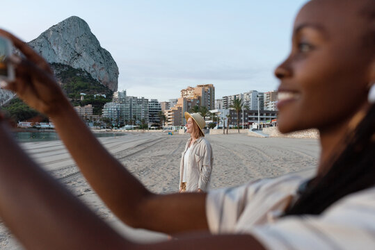 Woman resting on beach near black friend taking photo