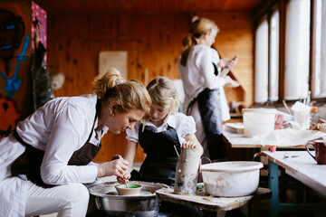 Girl with teacher painting clay bowl 