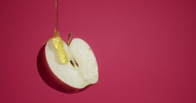 Pouring of sweet honey on half of ripe apple against color background