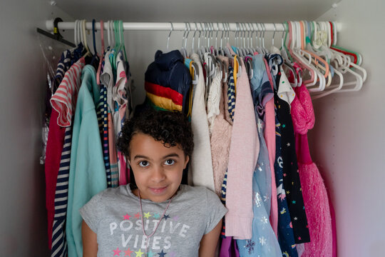 Camera aware Girl leans against clothes in closet