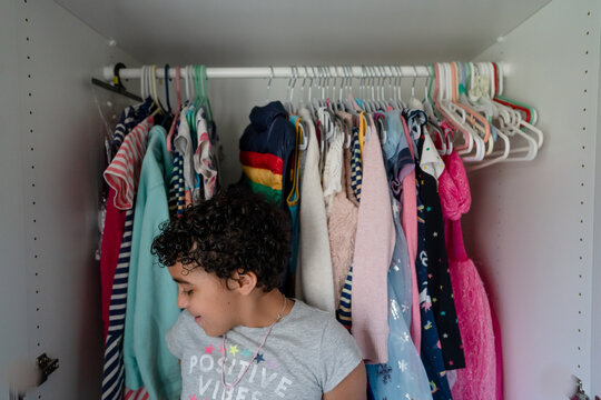 Girl leans against clothes in closet