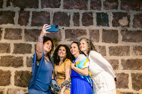 Content women taking self portrait on smartphone against brick wall