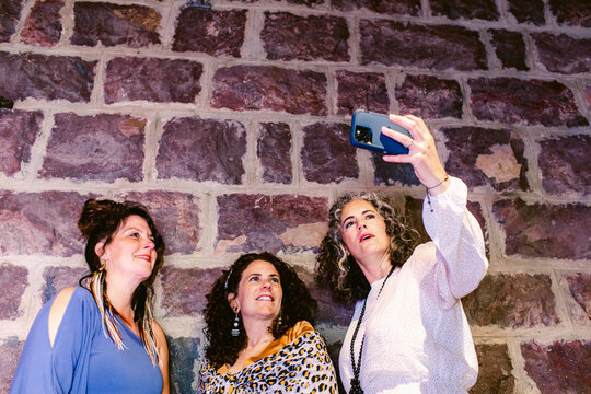 Content women taking self portrait on smartphone against brick wall