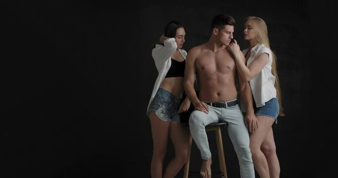 Handsome man and two beautiful women on dark background. Polyamory concept