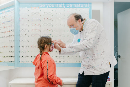Young girl wearing a face mask trying out glasses