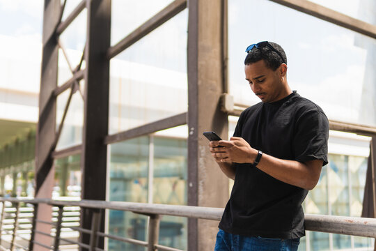 Hispanic guy browsing smartphone near railing