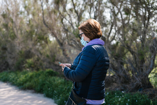 Woman in mask using smartphone in park