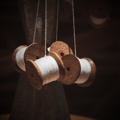 Selective focus foreground on hanging group of thread shabby bobbins with white cotton yarn on blurred dark brown background.Vintage wooden spools of white threads closeup. 