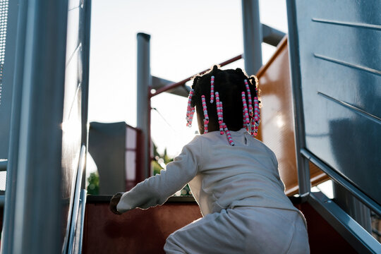 Anonymous girl climbing stairs in a playground at sunset.