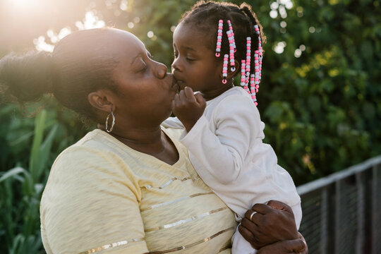 Black mother carrying and kissing daughter in park