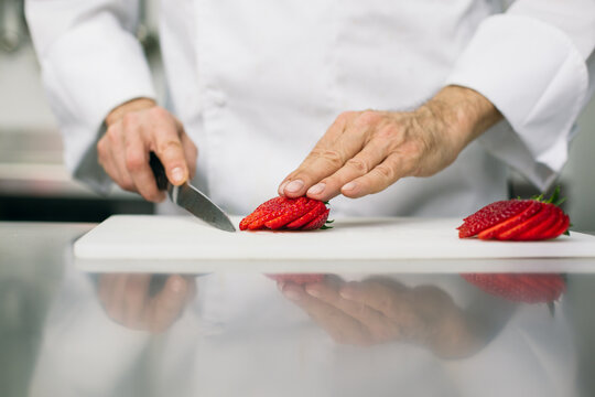 Chef slicing strawberries with kitchen knife 