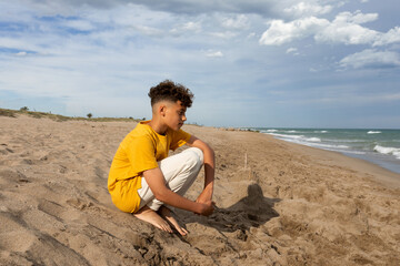 Teen boy sitting on the sand at the beach