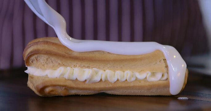 Chef cover the eclair with glaze choux cream. Decorating eclairs with vanilla cream. Glaze on eclair and profiteroles. Freshly baked crispy oblong eclairs. Traditional French eclairs with custard.