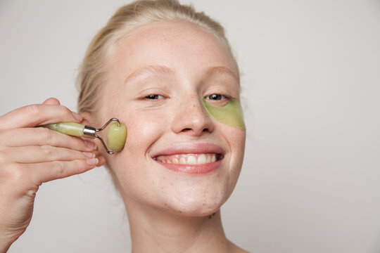Model with green jade roller and under-eye patch smiling
