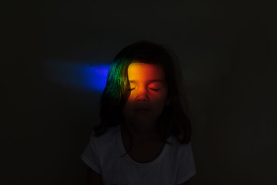 A child  in the dark with a rainbow prism on the face. 