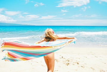 Blonde girl with rainbow towel at sunny beach with ocean