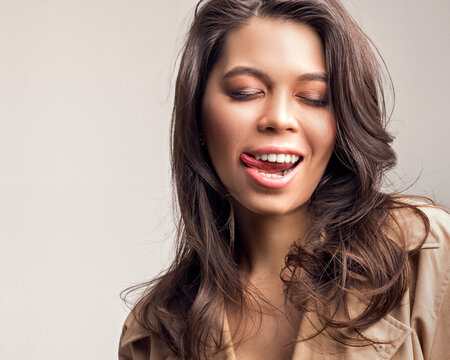 The woman licks her lips. Mmm... So tasty. Clean face and white teeth. 
Tongue touching upper lip. Female portrait with fashion make-up and with her hair down in the wind. Voluminous lush hairstyle.