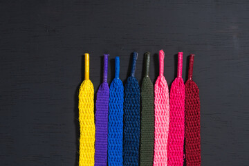 background of colored shoelaces on black wood, arranged vertically, concept of perfection, leaving space for advertising text