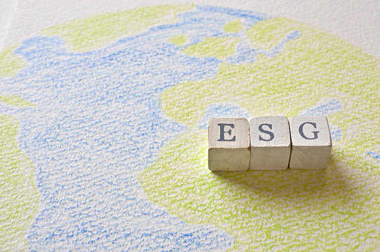 There is a cube stamped with the letters of the ESG on top of a sketchbook with a picture of the earth.