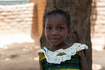 Portrait of a beautiful black preschool girl wearing a typical colourful African dress with white...