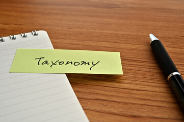 There is sticky note with the word of Taxonomy on the desk with a pen.