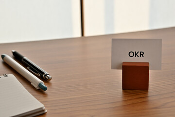 There is a card on paper stand with the word of OKR which is an abbreviation for Objectives and Key...