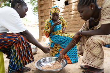 Black women sharing their meal according to West African rural tradition, sitting separeted from...