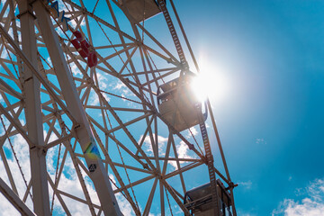 Ferris wheel and sun with clouds in the sky.