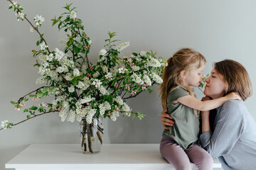 Mother and daughter hugging near flowers at home