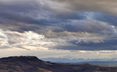 Obraz na płótnie Canvas Paese sulle colline grandi nuvole grigie in cielo sopra le valli e le montagne innevate