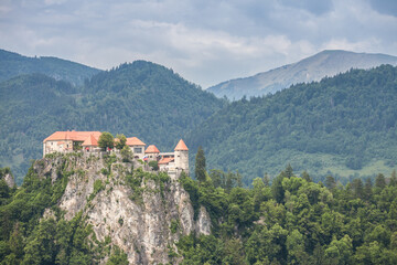 Fototapeta na wymiar Selective blur on the Bled castle, also called Blejski Hrad, during summer, surrounded by the trees of a green forest and the mountains of Julian alps. Bled Castle is a major monument of Slovenia