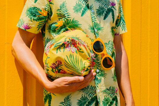 man in a hawaiian shirt, holds a matching bucket hat in his hand
