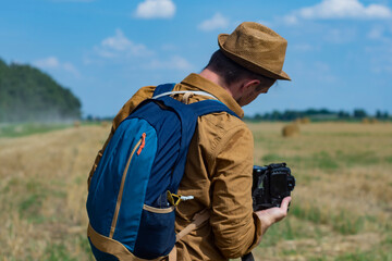 Traveler photographer with a camera in his hand against the background of a field and haystacks.