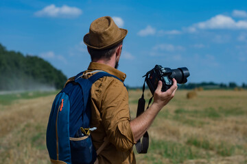 Traveler photographer with a camera in his hand against the background of a field and haystacks.