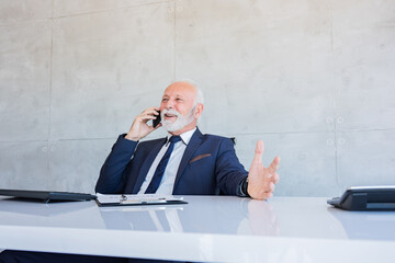 Happy bearded old businessman talking on his mobile phone while taking a break from work.