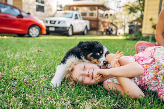 Girl laying in grass laughing at puppy licking her face