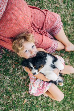 Overhead view of girl sitting in pregnant mom's lap holding australian shepherd puppy