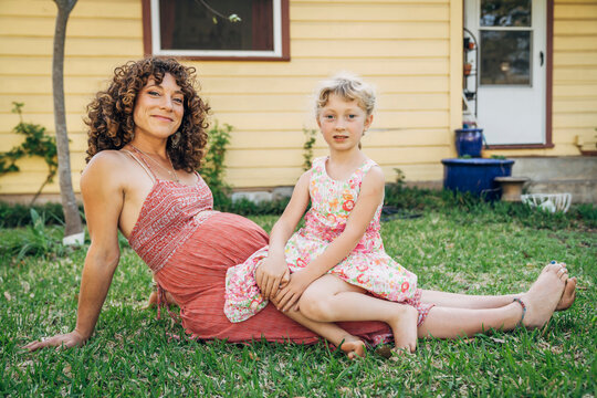 Portrait of girl sitting on pregnant mom's lap in yard