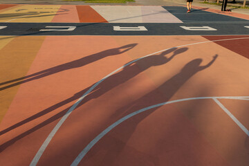 Shadows of children on a reddish basketball court
