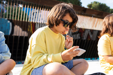 Cool boy eating a loliipop and uses his phone at street