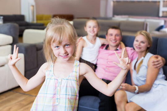 Postrait of happy girl kid is standing near new sofa in furniture store